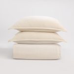 Amity home pure duvet cover and two shams in ivory stacked neatly showing a subtle woven texture