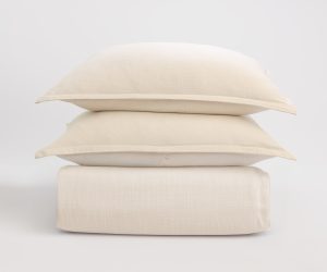 Amity home pure duvet cover and two shams in ivory stacked neatly showing a subtle woven texture