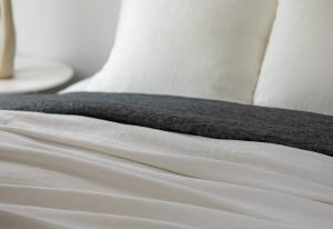 Amity home damara duvet cover   ivory with a soft wrinkled texture draped on a bed with a dark grey throw