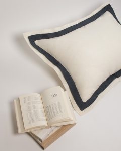 Amity home orfeo linen pillow sham in ivory with a steel blue contrasting border showing soft linen texture styled with a book