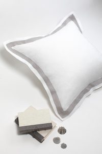 Amity home orfeo linen pillow sham in white with a grey border showcasing soft linen texture on a white surface styled with books and seashells