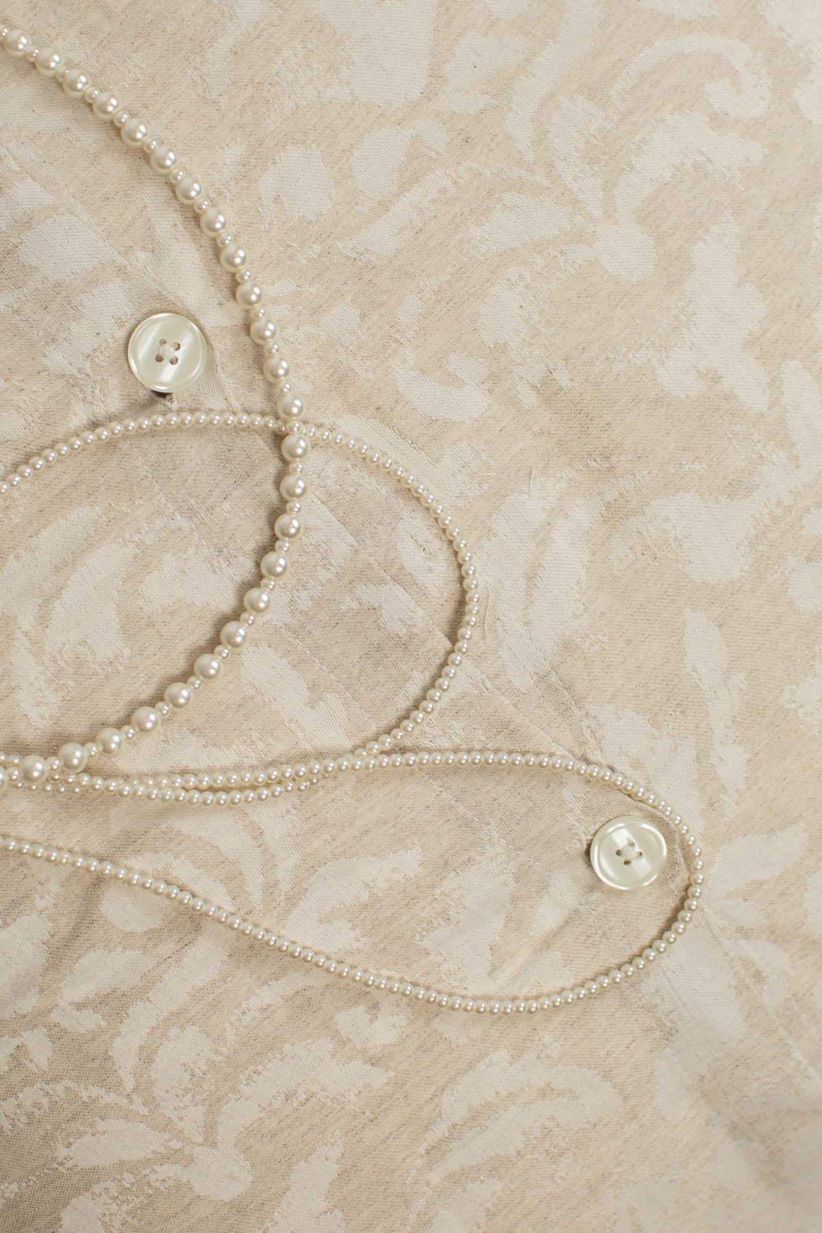 Amity home odette duvet cover   close up of light beige fabric with subtle woven jacquard floral pattern and mother of pearl buttons