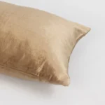Close up of a beige velvet pillow against a white background showing the soft fabric texture and corner seam