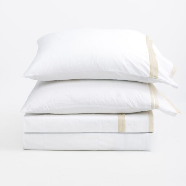 Stack of white pillows stacked on top of each other with beige seam tape against a plain white background, conveying a clean bedding scene.