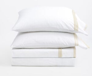 Stack of white pillows stacked on top of each other with beige seam tape against a plain white background conveying a clean bedding scene