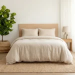 Minimalist bedroom with beige bedding a light wood headboard a tall green plant in a woven basket on the left and white curtains on the right