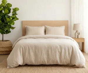 Minimalist bedroom with beige bedding a light wood headboard a tall green plant in a woven basket on the left and white curtains on the right