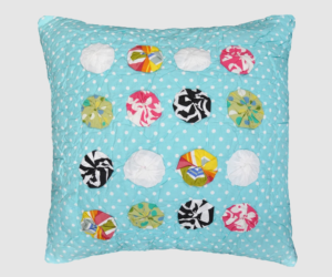 Decorative square pillow with blue polka dot fabric and multicolored circular patchwork circles