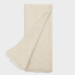 Cream bath towel with fringed edges partially folded across a flat surface