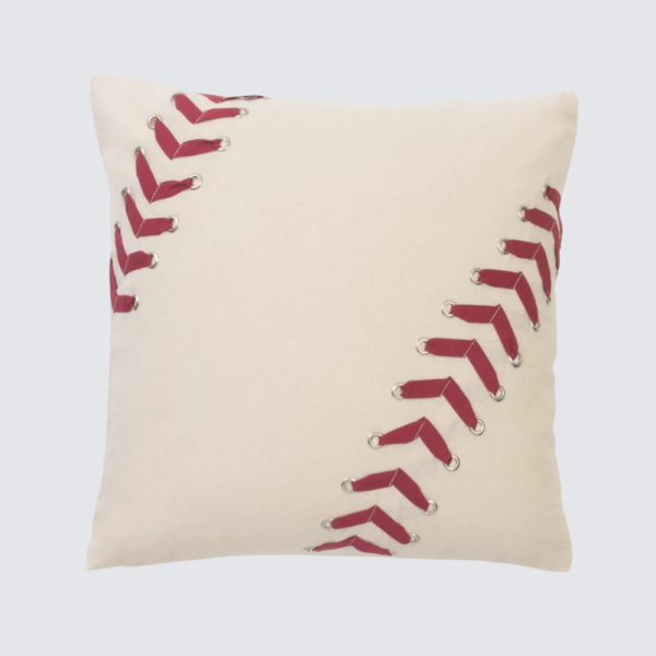 Beige decorative pillow with red baseball‑stitch style lacing along diagonal seams on cream fabric.