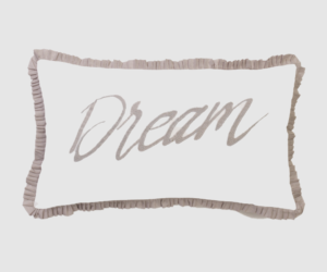 Decorative white pillow with beige ruffled edges and the word dream in cursive centered on the front