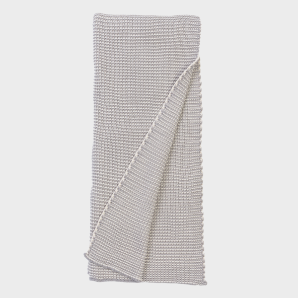 Light gray knitted throw blanket folded with a corner draped over the edge.