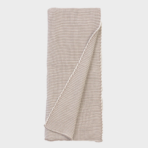 Beige knitted throw blanket folded neatly with a corner draped over the edge on a white background