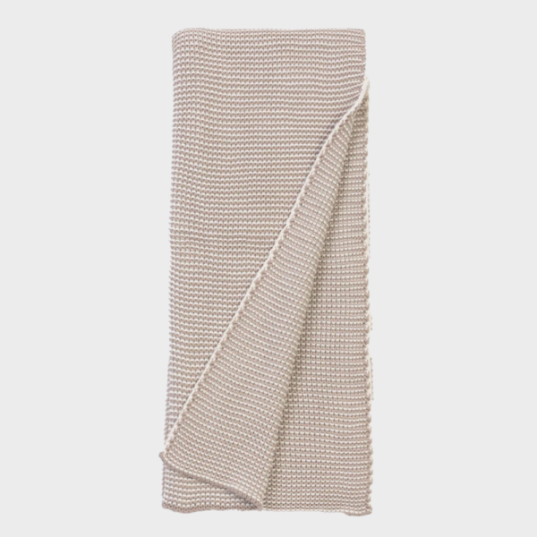 Beige knitted throw blanket folded neatly with a corner draped over the edge on a white background