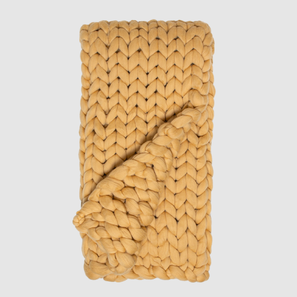 Mustard-yellow chunky-knit scarf folded with oversized interwoven stitches showing a looped end.