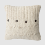 Cream knitted throw pillow with cable patterns and dark buttons along the front edge