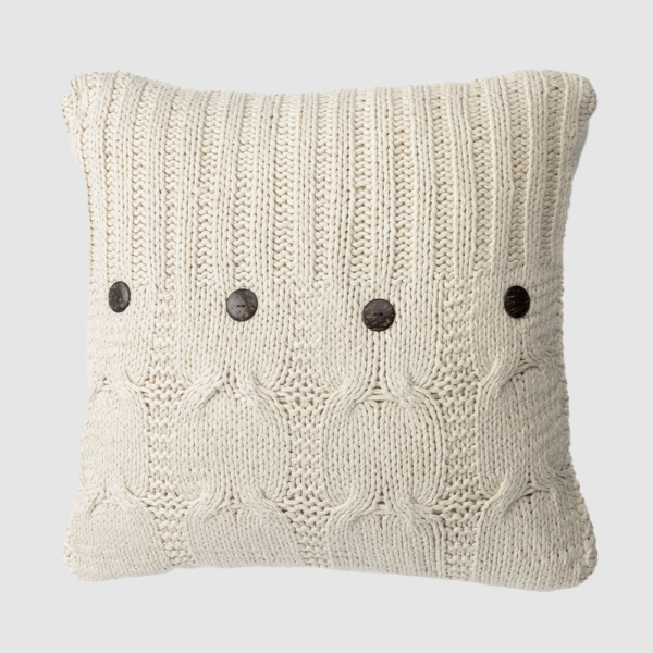 Cream knitted throw pillow with cable patterns and dark buttons along the front edge