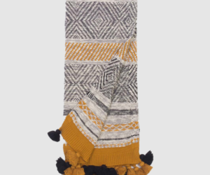Woven throw blanket with black white and mustard geometric patterns and navy tassels along the edges