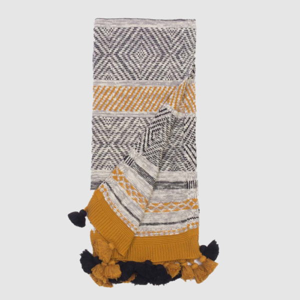 Woven throw blanket with black, white, and mustard geometric patterns and navy tassels along the edges.
