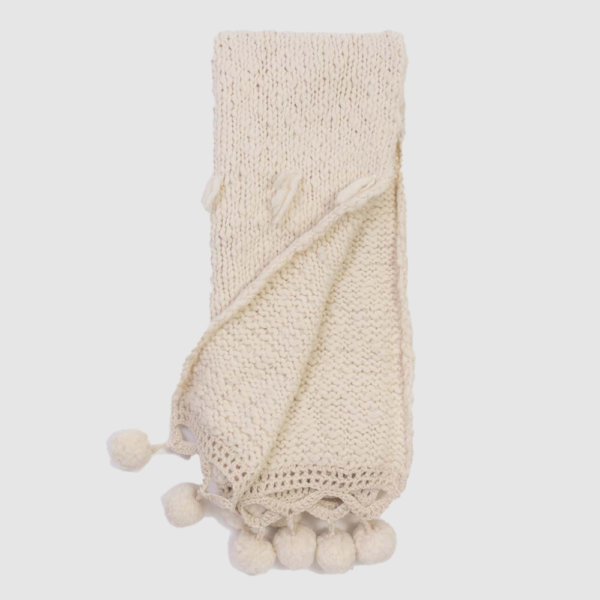 Cream knitted scarf with tassels and pom-pom fringe along the edge.