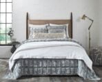 Bedroom scene with a made bed white bedding and blue gray pillows against a white brick wall a brass floor lamp on the right