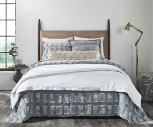 Bedroom scene with a made bed white bedding and blue gray pillows against a white brick wall a brass floor lamp on the right