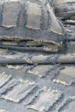 Close up of stacked blue denim fabric swatches with frayed hems and visible weaving patterns displaying texture and fringe edges