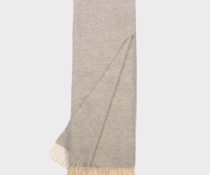 Light gray scarf with cream fringe along both ends laid flat with one corner slightly folded
