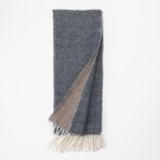 Dark blue denim scarf with a beige underside and white fringe folded flat on a white background