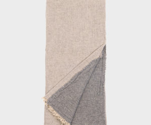 Beige folded throw blanket with a gray fringed underside showing on the corner edge