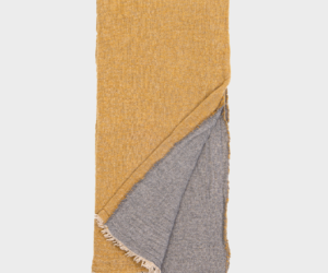 Mustard yellow throw blanket folded to reveal a grey reverse side with cream fringe along the edges