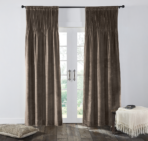 Brown velvet curtains hung over white french doors with light filtering through a cushioned floor pillow on the left and a fringed throw with books on a small table to the right