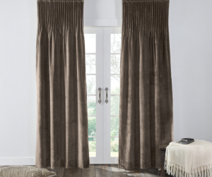 Brown velvet curtains hung over white french doors with light filtering through a cushioned floor pillow on the left and a fringed throw with books on a small table to the right