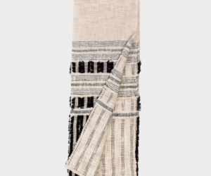 Beige woven throw blanket with black and navy stripes folded with a corner pulled back