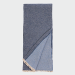 Folded blue denim scarf with light fringe along the ends shown against a light background