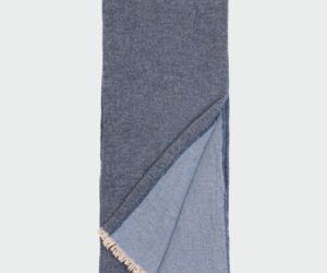 Folded blue denim scarf with light fringe along the ends shown against a light background