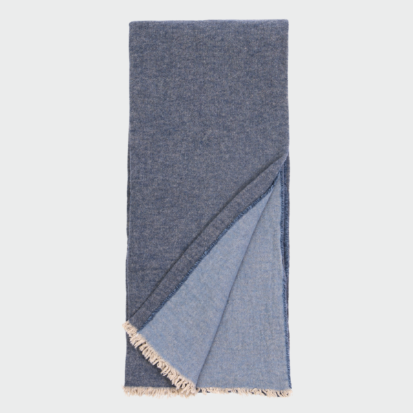 Folded blue denim scarf with light fringe along the ends, shown against a light background.
