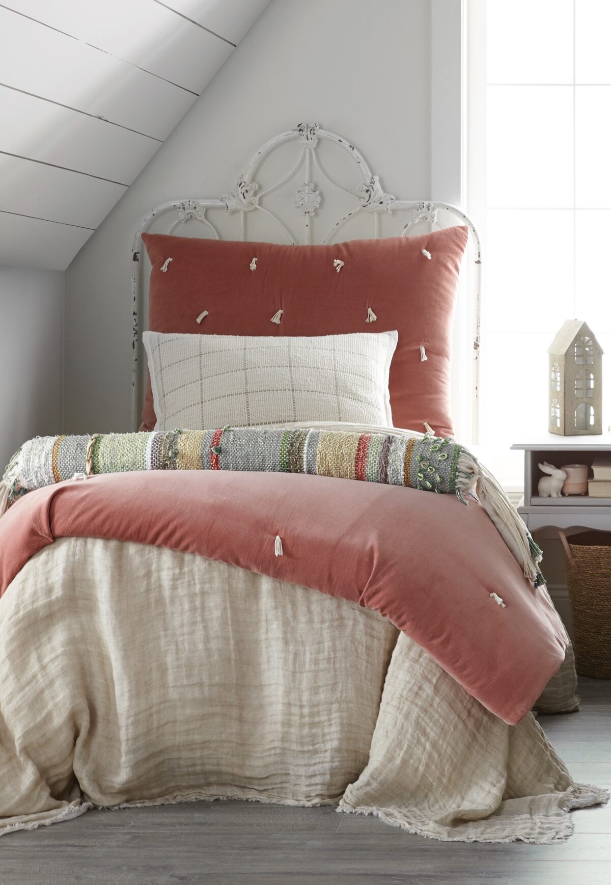 Rust pink tufted comforter on a distressed white metal bed frame in a bright cozy bedroom