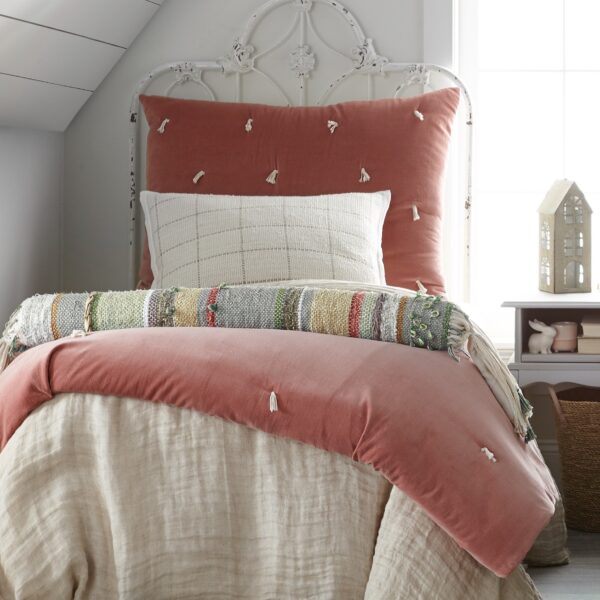 Rust pink tufted comforter on a distressed white metal bed frame in a bright cozy bedroom