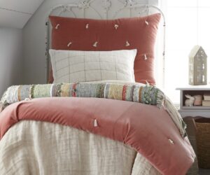 Rust pink tufted comforter on a distressed white metal bed frame in a bright cozy bedroom