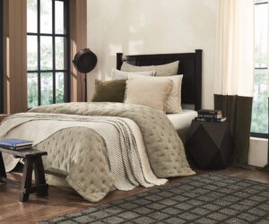 Cozy bedroom with a tufted beige quilt cream pillows and a dark wood headboard by large sunlit windows