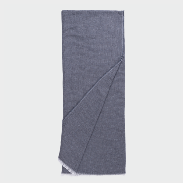 Blue knit scarf folded with fringe at one end, laid flat against a light background