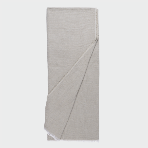 Light gray woven throw blanket folded with a corner flipped over, showing fringed edge on a plain background