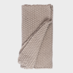 Beige chunky knit blanket folded and draped for a cozy look textured yarn loops visible in close up