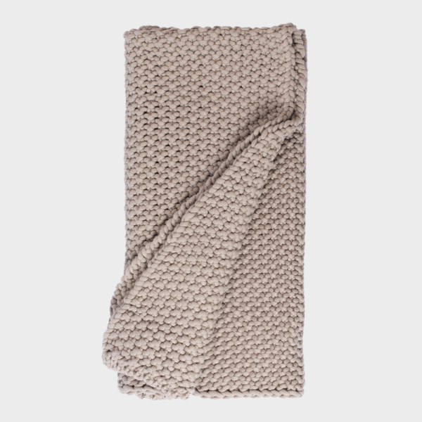 Beige chunky knit blanket folded and draped for a cozy look, textured yarn loops visible in close-up