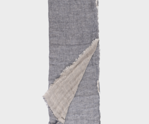Blue gray linen scarf with frayed edges partly folded to reveal a beige underside