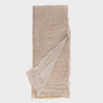 Beige linen fabric laid flat with a fringed edge one corner folded back to show the lighter underside