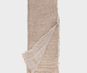 Beige linen fabric laid flat with a fringed edge one corner folded back to show the lighter underside