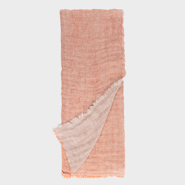 Peach-colored woven scarf with frayed edges, one corner folded over to reveal a lighter underside.