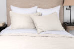 Bed with white and beige pillows and a cream blanket in a neutral toned bedroom